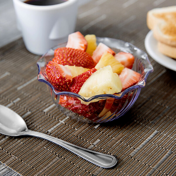 A clear glass bowl filled with fruit on a table with a spoon.