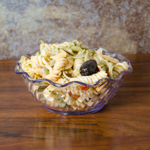 A clear swirl tulip bowl filled with pasta and olives.