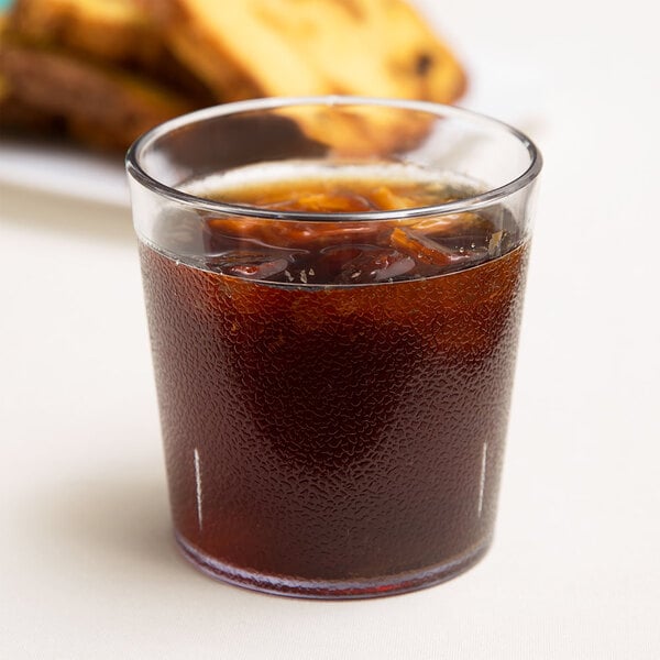 A close up of a Dinex clear plastic tumbler filled with a brown beverage and ice.