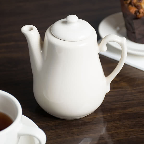 A white Homer Laughlin Seville beverage server on a table next to a cup of tea.