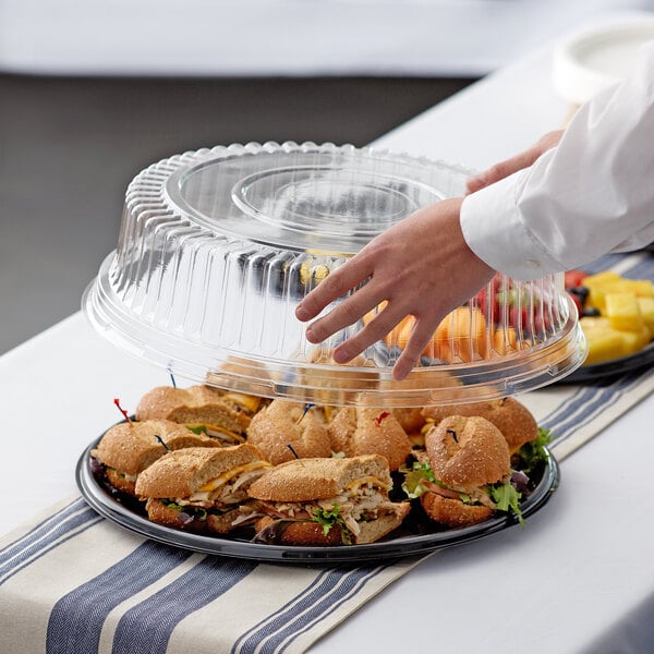 A person holding a Visions clear plastic catering tray with food on a table.