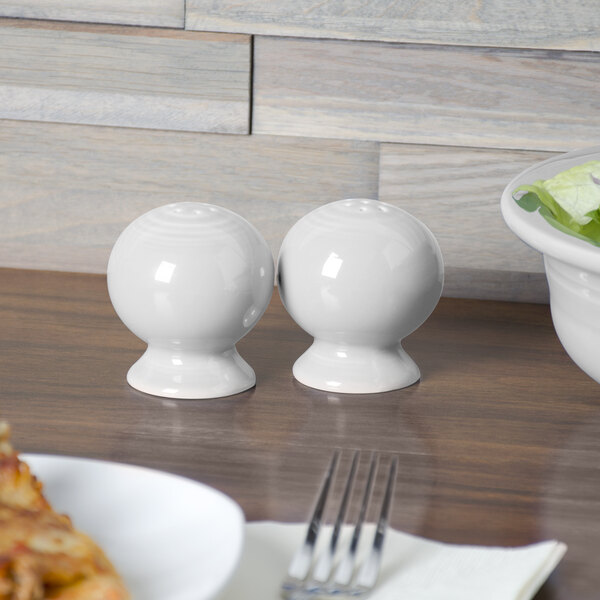 A white round Fiesta pepper shaker on a wood surface.