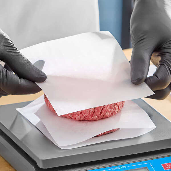 A stack of square patty papers being used to separate raw hamburger patties.