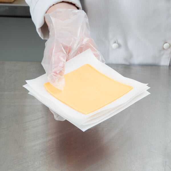 A person in a white glove using Choice patty paper to hold a piece of cheese.