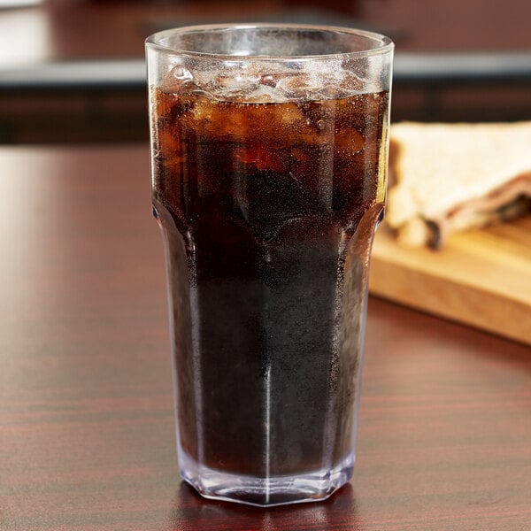 A Carlisle clear plastic tumbler filled with brown liquid and ice on a table.