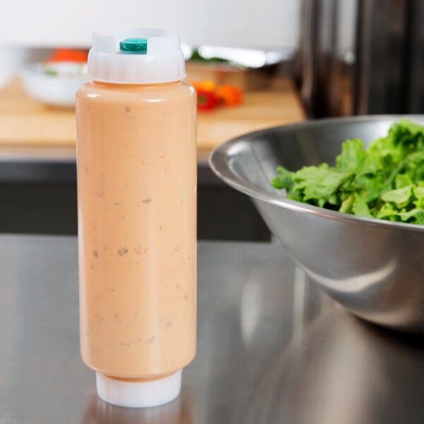 A white plastic FIFO squeeze bottle of sauce next to a bowl of green lettuce.