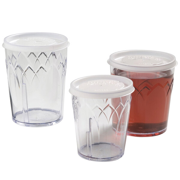 A clear plastic Dinex tumbler lid with a straw slot over a clear plastic tumbler.