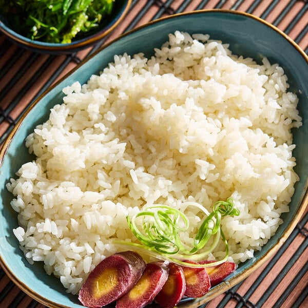 A bowl of cooked medium grain white sushi rice garnished with sliced vegetables and greens.