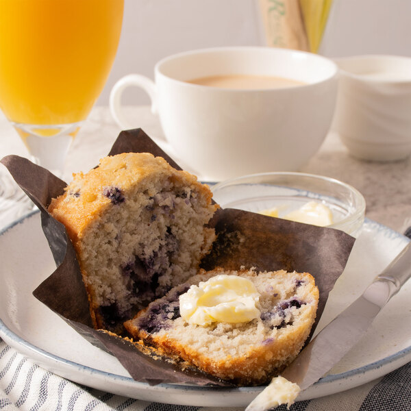 A plate with a muffin and butter next to a glass of orange juice.