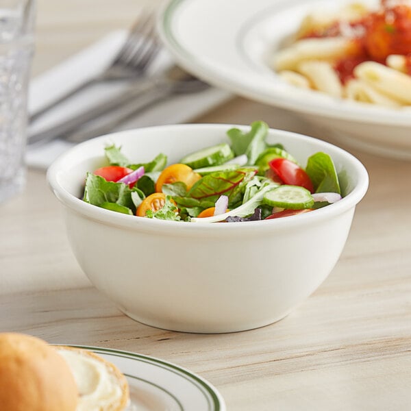 A Tuxton eggshell white china bowl filled with salad on a table.