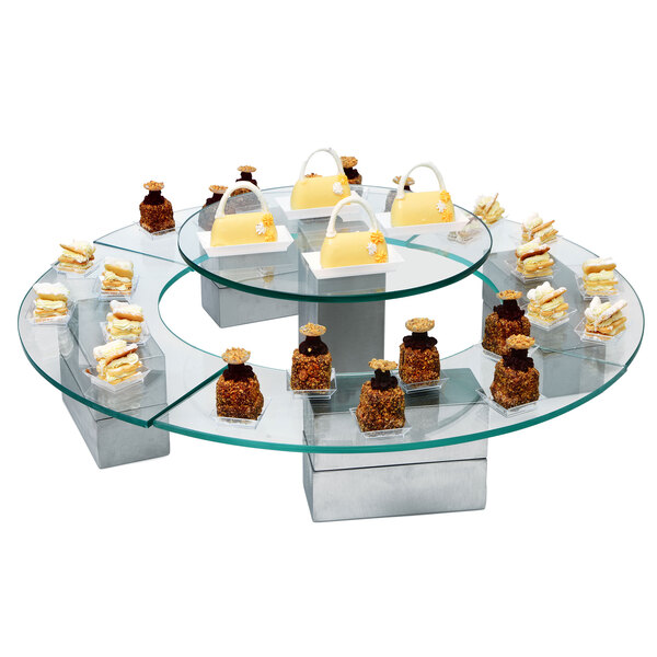 An Eastern Tabletop quarter circle acrylic buffet shelf with a display of cakes and desserts on a glass table.
