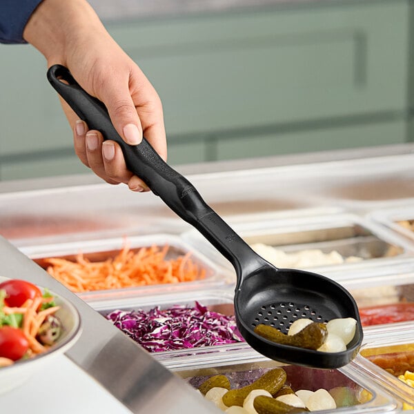 A hand using a black Vollrath Spoodle to serve food from a salad bar.