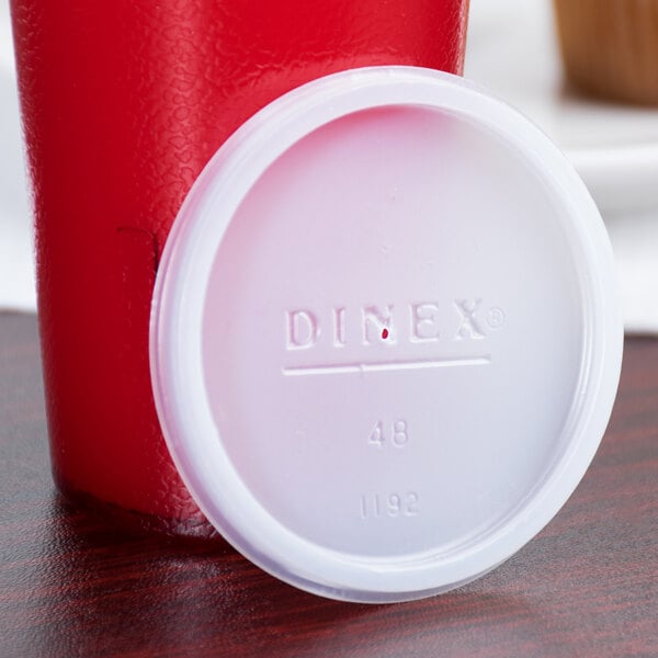 A white plastic lid for a Dinex juice cup sitting on a table.