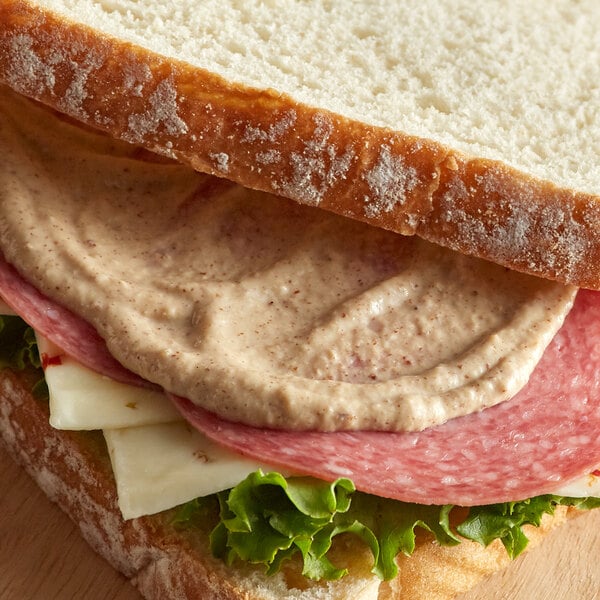 A sandwich with meat and cheese on a piece of bread with Admiration Dijon Mustard.