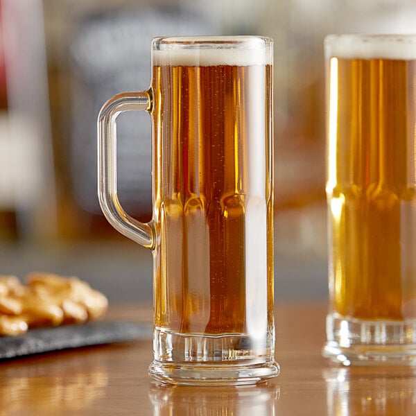 Two Libbey Frankfurt beer tasting mugs filled with yellow liquid on a table in a bar.