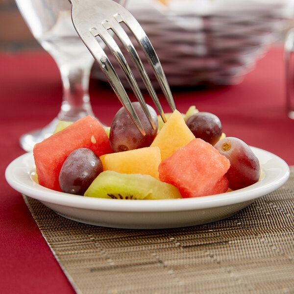 A fork holding a piece of fruit on a Tuxton Colorado narrow rim china plate.
