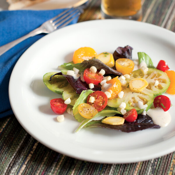 A Tuxton Colorado bright white narrow rim china plate with a salad on it, with a fork.