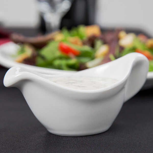 A white sauce in a Tuxton white china gravy boat.