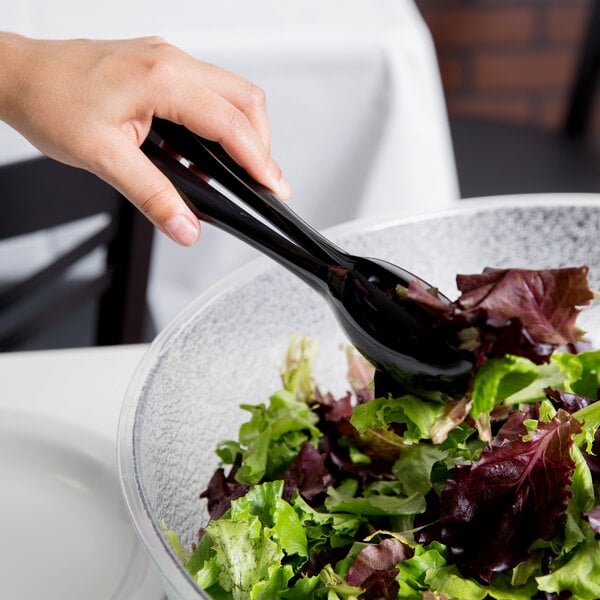 A pair of black disposable plastic tongs being used to serve salad from a bowl.