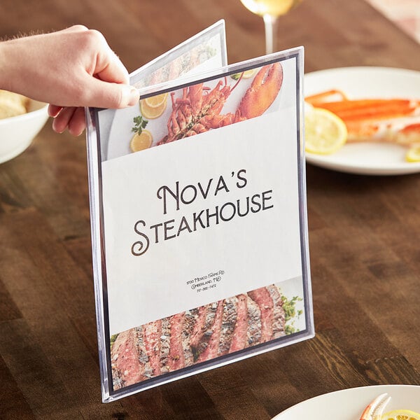 A person holding a clear menu with a white plate of cooked lobster on a table.