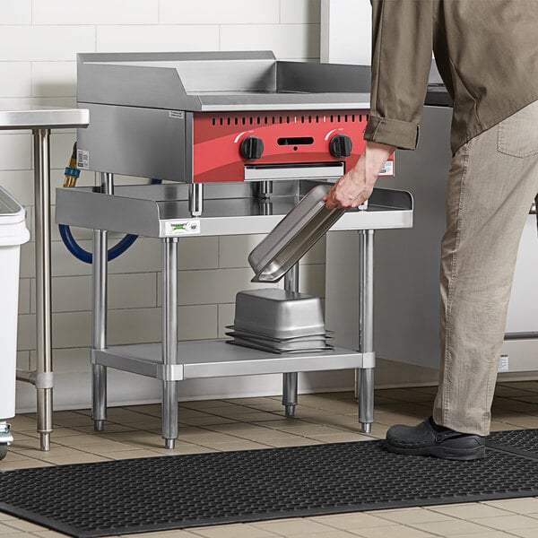 A man stands near a Regency stainless steel equipment stand in a professional kitchen.