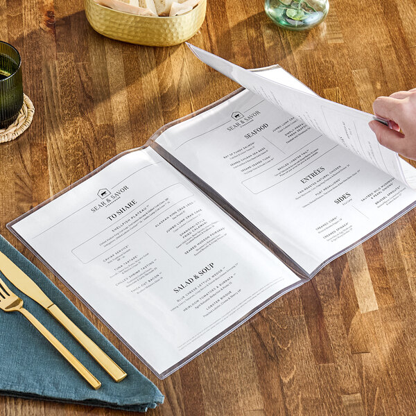 A person holding a clear menu on a table.