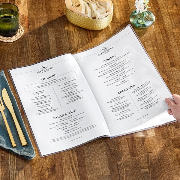 A person holding a clear menu on a brown table.