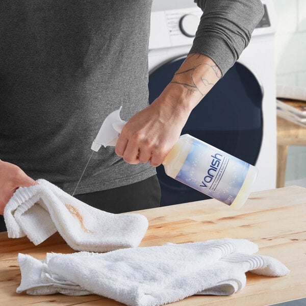 A person using Noble Chemical Vanish Laundry Pre-Spotter to spray a white towel.