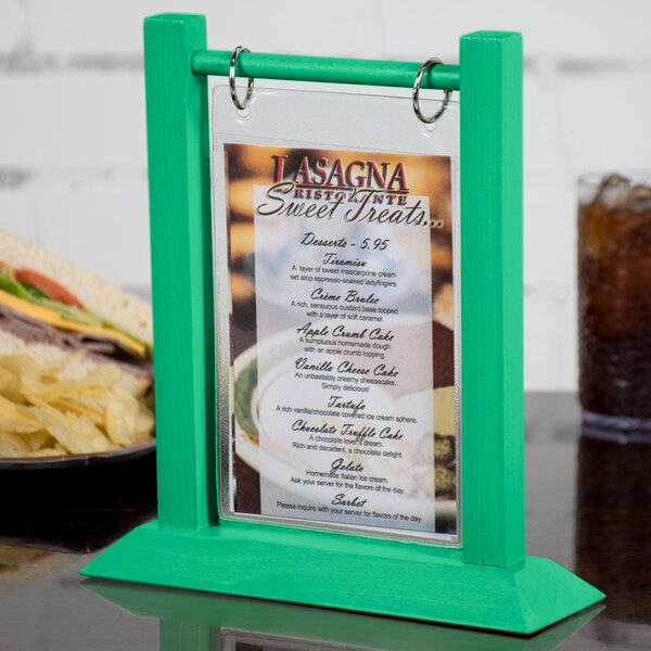 A teal wood flip top table tent holding a menu on a table with a sandwich and chips.