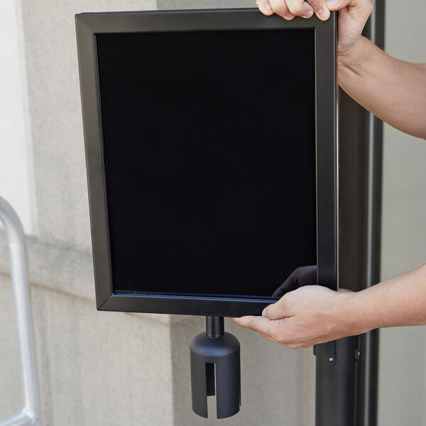 A person holding a black rectangular Aarco sign frame.