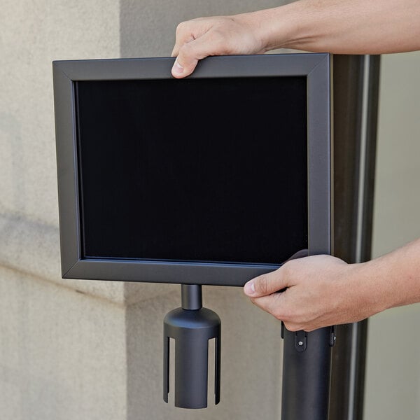 A person holding a black Aarco stanchion sign frame on a pole.