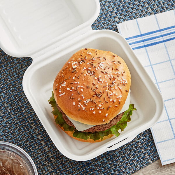 An EcoChoice bagasse takeout container with a hamburger inside on a table.