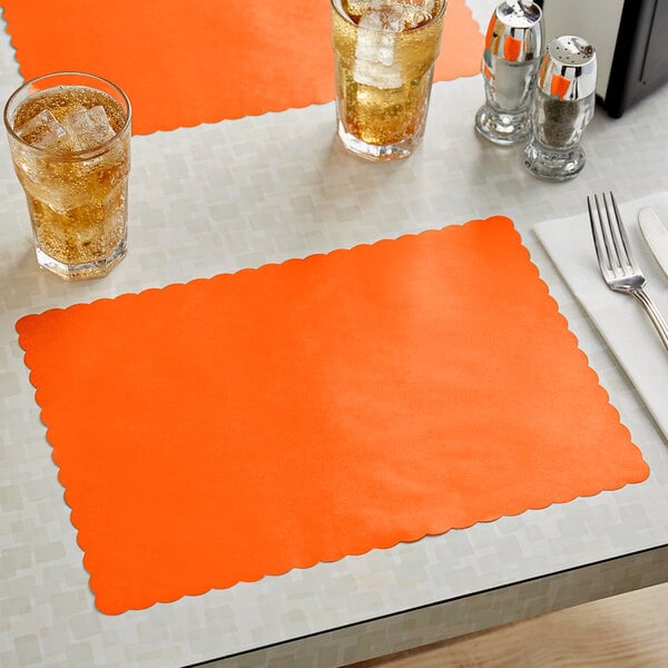 A bittersweet orange scalloped paper placemat on a table with glasses of liquid and silverware.