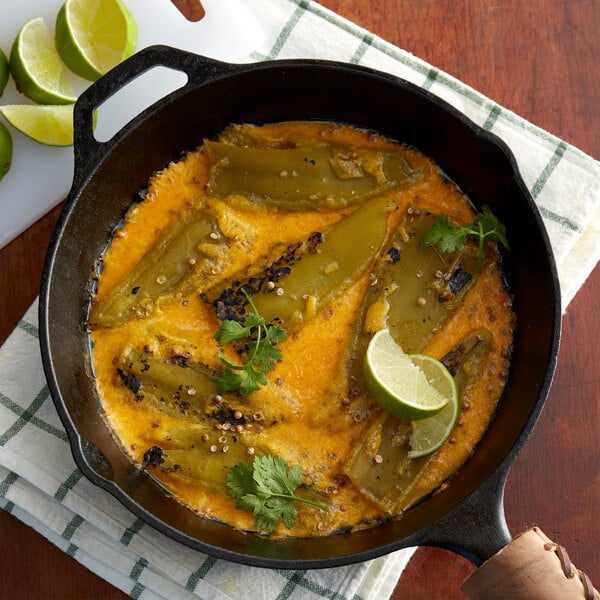 A black skillet of food with green chile peppers and lime slices on a table.