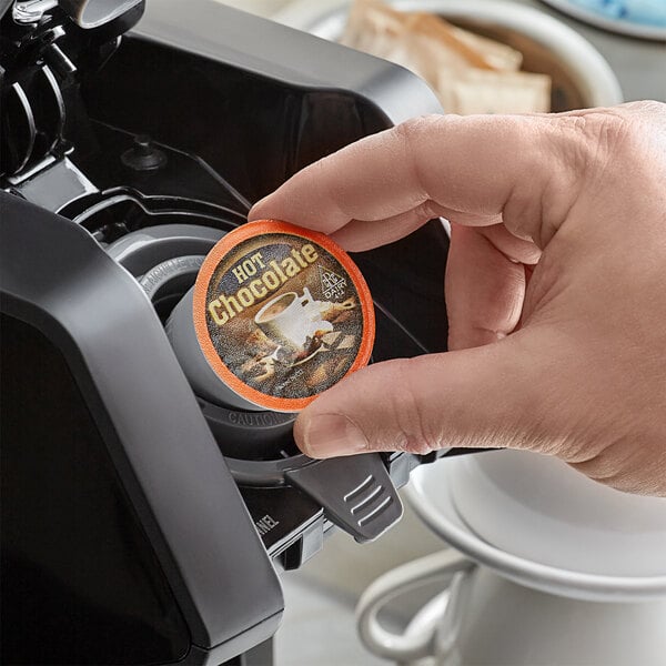 A hand holding a round container of Caffe de Aroma hot chocolate with a label.