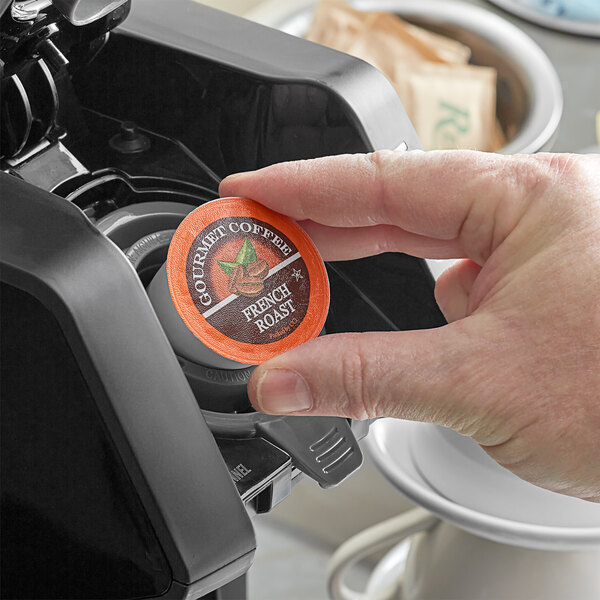 A hand holding a Caffe de Aroma French Roast coffee single serve cup.