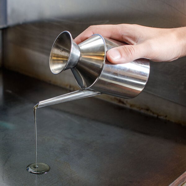 A hand pouring liquid from a Town stainless steel oil dispenser.