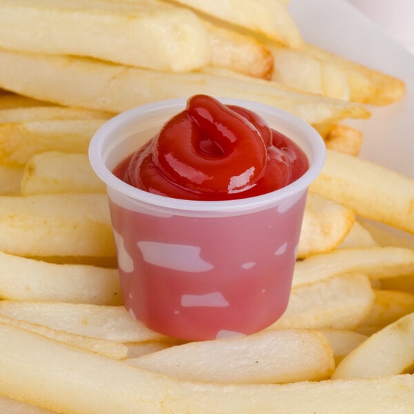 A Solo translucent polystyrene souffle cup of ketchup on french fries.