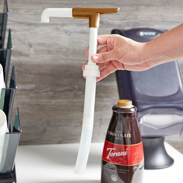 A hand using a white Torani pelican sauce pump to dispense syrup into a coffee cup.