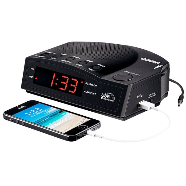 A black Conair alarm clock with a cell phone charging on it.