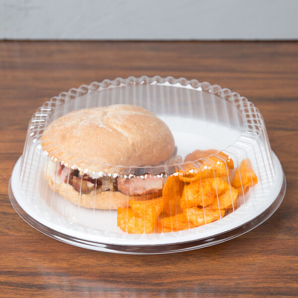 A Dart clear plastic dome plate cover over a plate with a sandwich and potato chips.