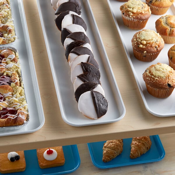 A white Cambro market tray of pastries and muffins on a bakery display counter.