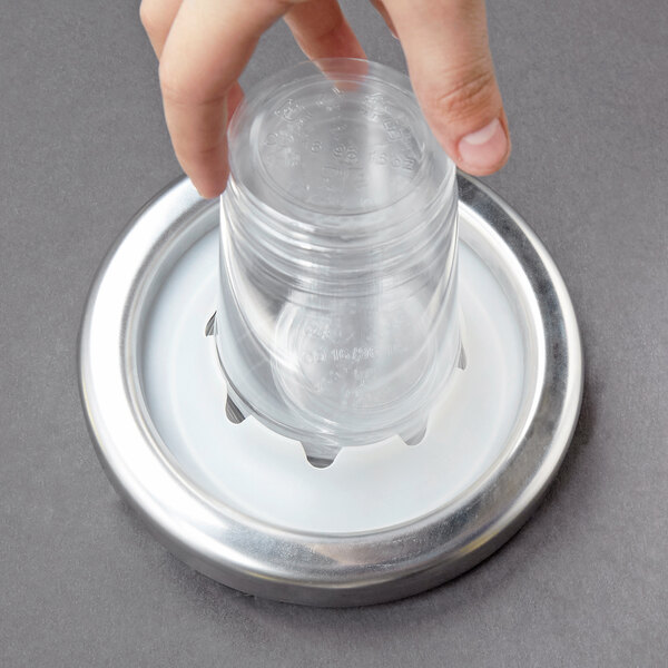 A hand using a Carlisle large cup dispenser gasket to fill a plastic cup on a metal tray on a counter.