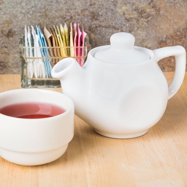 A white Tuxton china teapot and a cup of tea.