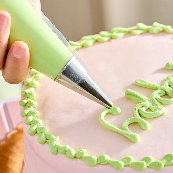 A metal piping tip being used to decorate a cake with green icing.