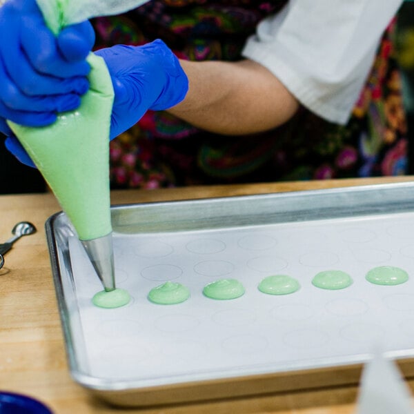 A person using an Ateco plain piping tip to pipe green pastry.
