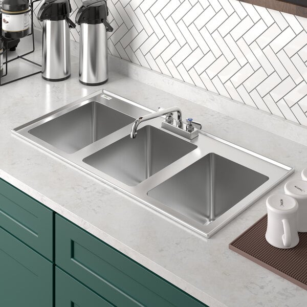 A Regency stainless steel three compartment drop-in sink with a faucet above it.