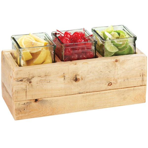 A Cal-Mil wooden box display with 3 glass jars filled with lemons, limes, and cherries.