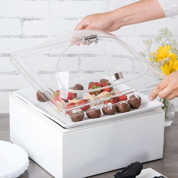 A person holding a Cal-Mil glass container with strawberries and chocolate inside.