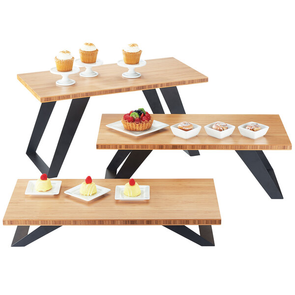 A bamboo stair-step riser on a table with three wooden tables displaying desserts on them.